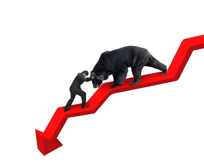 Photo of a businessman pushing against a bear trying to walk on a red downward trend line.