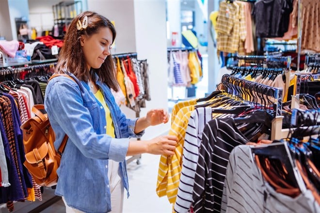 Woman in clothes store looking at shirts on hangers — Photo