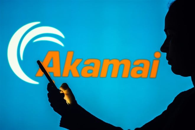 Akamai Technologies logo is seen in the background of a silhouetted woman holding a mobile phone