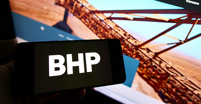 Person holding smartphone with logo of mining, metals and petroleum company BHP Group on screen in front of website. 