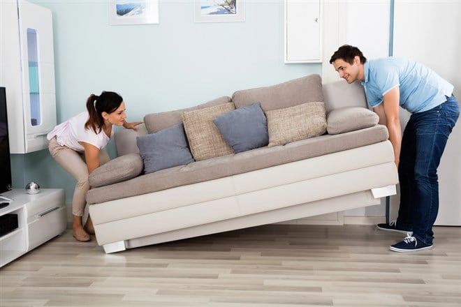 Photo of a couple placing a soft down in their living room, sofa at an upward angle stymbolizing rising stock prices.