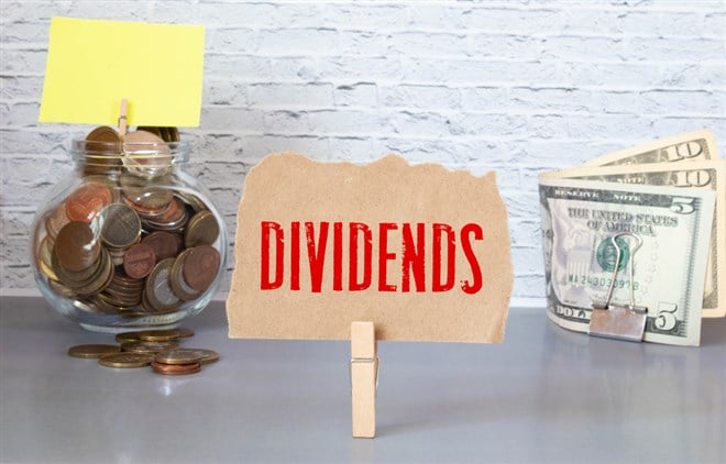 Hand putting coin in jar word dividend with money stack, Concept business finance and investment.