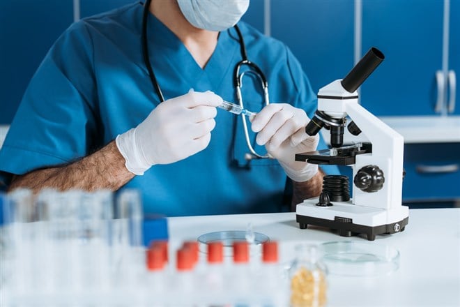 Cropped view of biologist in medical mask and latex gloves holding syringe near microscope — Photo