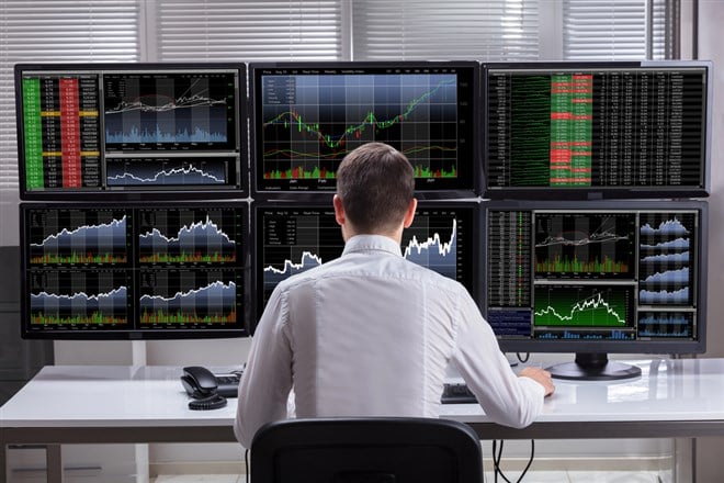 Photo of a stock trader sitting in front of 6 computer screens showing charts