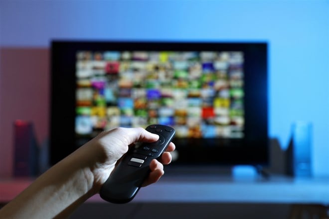 Woman switching channels on TV set with remote control at home, closeup