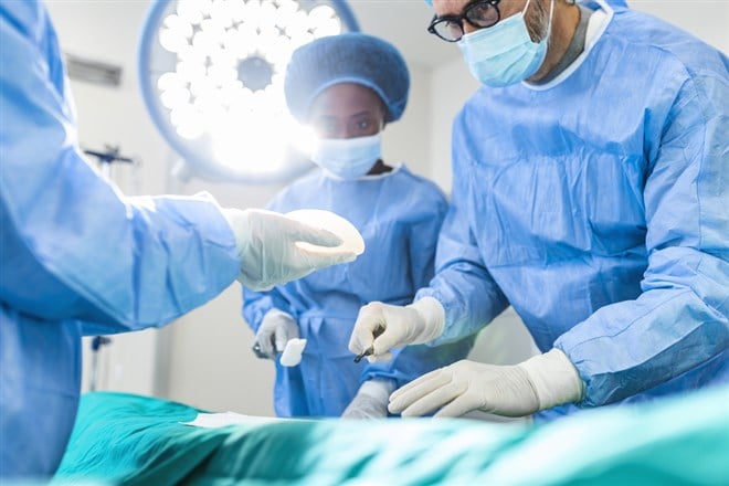 Surgeon and his assistant performing cosmetic surgery in hospital operating room. Surgeon in mask during medical procadure. Breast augmentation, enlargement, enhancement