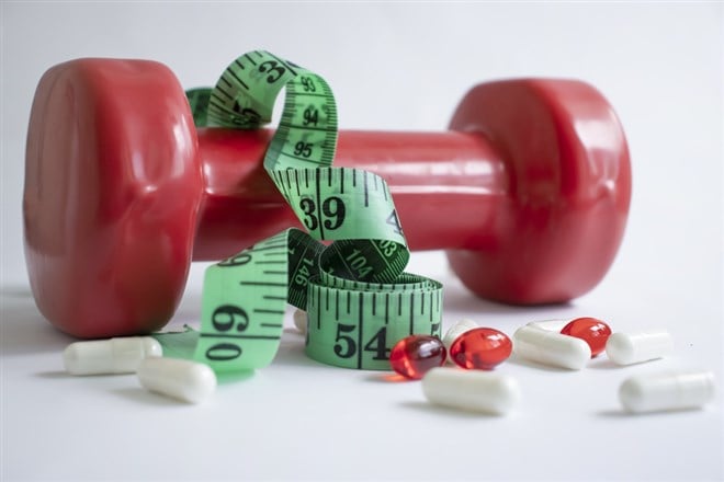 Dumbbells, measuring tape, weight loss pill capsules on a light background - stock image