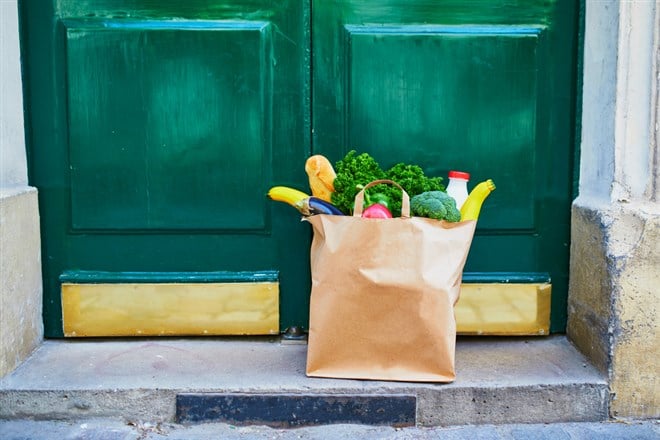 Food delivery during coronavirus outbreak. Paper bag with grocery order in front of the door in Paris, France during Covid-19 epidemic. Safe online shopping, food donation or takeout meal concept