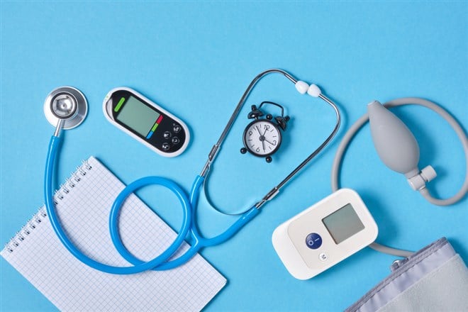 Digital blood pressure monitor, glucometer, stethoscope, notepad and alarm clock on blue background top view — Photo