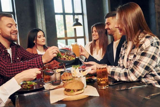 At daytime. Group of young friends sitting together in bar with beer.