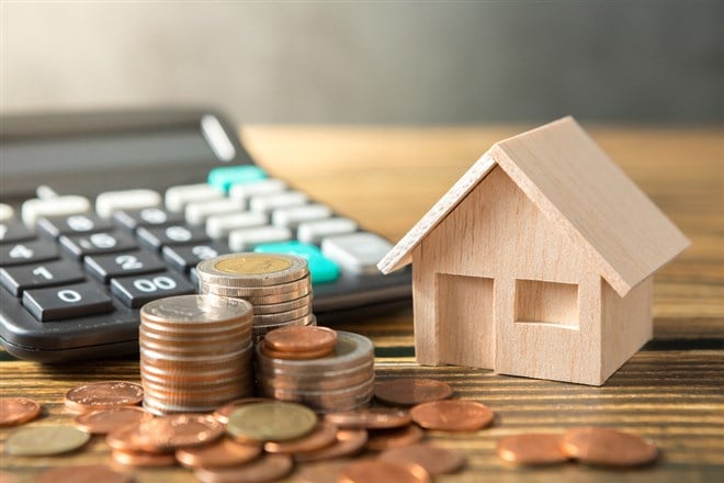 Model house, coins stack, calculator on wooden desks and loft walls with sunlight and copy space for money saving concept