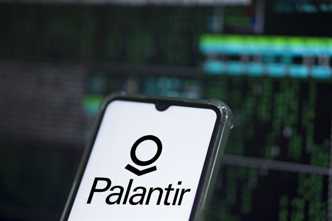 Palantir company logo on the screen of smartphone, finger touching it and the blurred Palantir logo on the background.