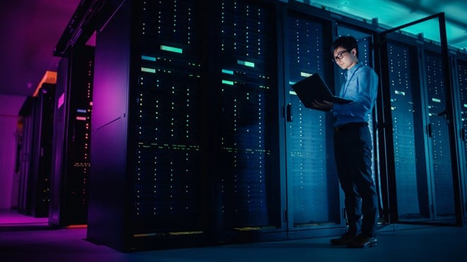 In Data Center: Male IT Technician Running Maintenance Programme on a Laptop, Controls Operational Server Rack Optimal Functioning. Modern High-Tech Operational Super Computer in Neon Colours, Lights — Photo