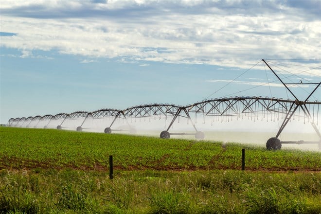 Irrigation machine watering the growing crop, on a clear day with some clouds in the sky. — Photo