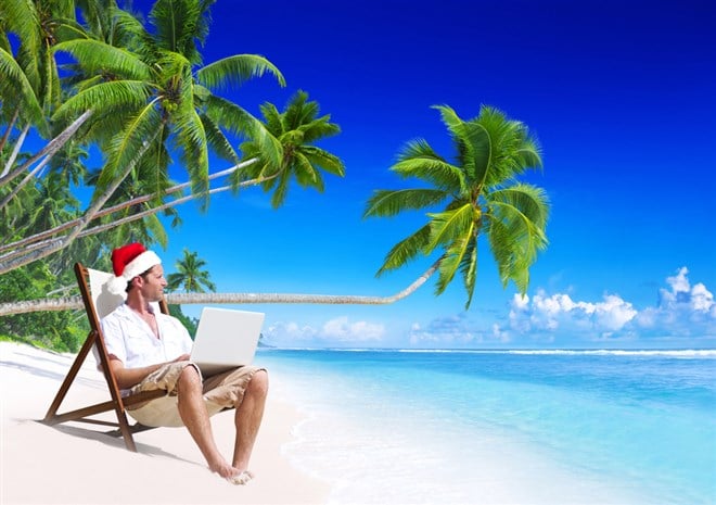 Photo of a man on a beach wearing a santa hat working on his laptop