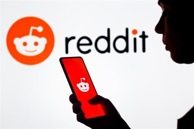 March 28, 2022, Brazil. In this photo illustration, a woman's silhouette holds a smartphone with the Reddit logo displayed on the screen and in the background