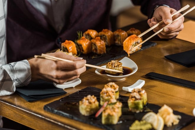 Cropped view of people dipping sushi rolls in soy sauce in restaurant — Photo