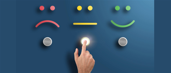 Photo of 3 smiley faces: red sad one; yellow neutral one; green happy one - each with a button below it. A finger is pushing the middle button, and its lit up.