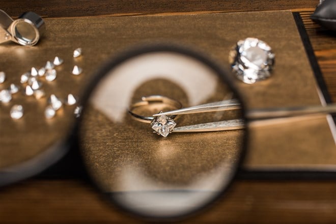 Selective focus of magnifying glass, jewelry ring with gemstone in tweezers on board on wooden table — Photo