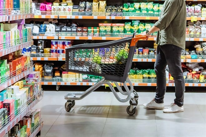 Young man with shopping cart between store shelf - stock image