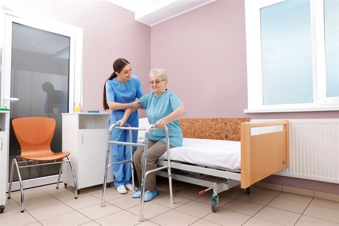 Nurse assisting senior woman with walker to get up from bed in hospital ward — Photo