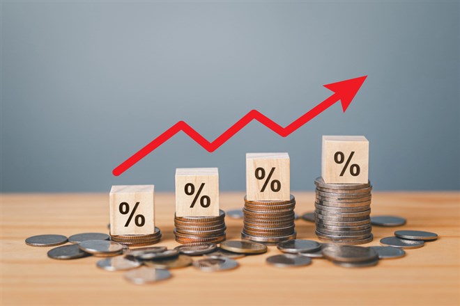 Inflation concept photo: red graph arrow, percent sign on a wooden cube with row of coins in idea for interest rate hike, world economics, and inflation control.