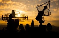 Silhouettes of satellite dishes or radio antennas against sunset sky. Space observatory