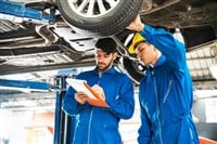 Mechanic in blue workwear uniform inspects the car bottom with his assistant. Automobile repairing service