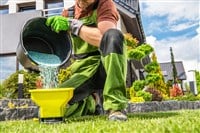 Caucasian Garden Worker Preparing Grass Lawn Fertilizer. Spring Time Fertilizing Job.