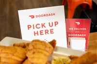 A view of a DoorDash pick up here sign on a table, and food in the foreground