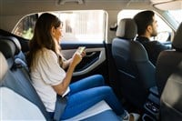 Side view of an attractive latin woman sitting on the car back seat and using a ride share app on her smartphone 