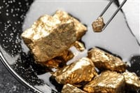 Tweezers with gold nugget above pile on grey table, closeup