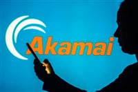 Akamai Technologies logo is seen in the background of a silhouetted woman holding a mobile phone