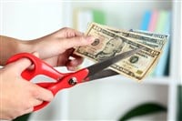 Hands with scissors cutting dollar banknotes, on blurred interior background