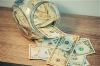 Dollar banknotes on the table, falling from glass jar, toned image. Saving money for a big and important purchase concept