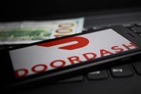 Close up of mobile phone screen with logo lettering of Doordash payment provider on computer keyboard