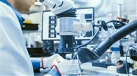 Close-Up Photo of an Electronics Factory Worker in White Work Coat Soldering a Printed Circuit Board Through a Digital Microscope