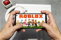 Photo on two hands holding a smartphone playing Roblox