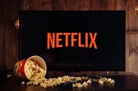 Photo of a Netflix logo on a TV screen, a container of spilled popcorn across the table in front of it.