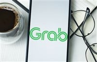 Photo of a cell phone with Grab logo, cup of coffee, and reading glasses