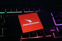 Closeup of mobile phone screen with logo lettering of crowdstrike cyber security company on computer keyboard (focus on upper part of bird logo)