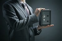 Photo of a man in a suit holding a safe; symbolizing a safe investment.