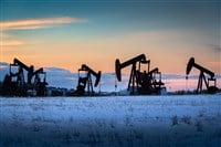 Oil and gas pump jacks working on a snow covered field at sunset in Rocky View County Alberta Canada.