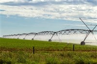 Irrigation machine watering the growing crop, on a clear day with some clouds in the sky. — Photo