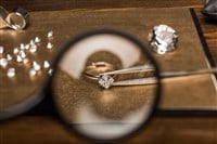 Selective focus of magnifying glass, jewelry ring with gemstone in tweezers on board on wooden table — Photo