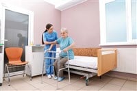 Nurse assisting senior woman with walker to get up from bed in hospital ward — Photo