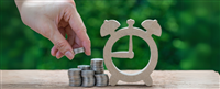 Photo of a woman's hand putting on stack of coins next to a wooden clock